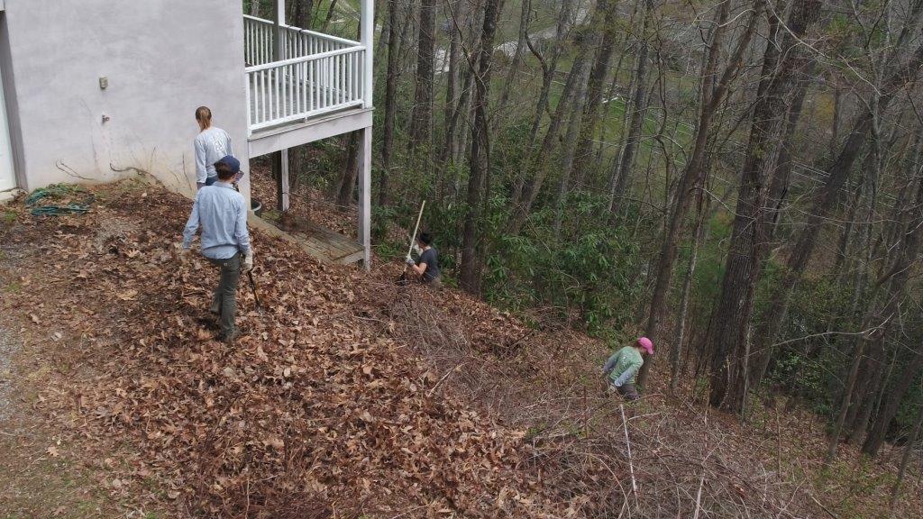 Four people remove brush alongside a house on a hillside