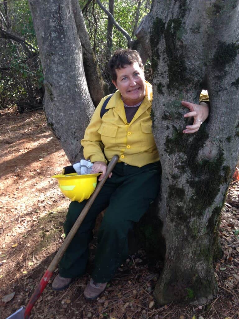 Photo of Sarah McCaffrey in yellow and green fire gear leaning against a tree