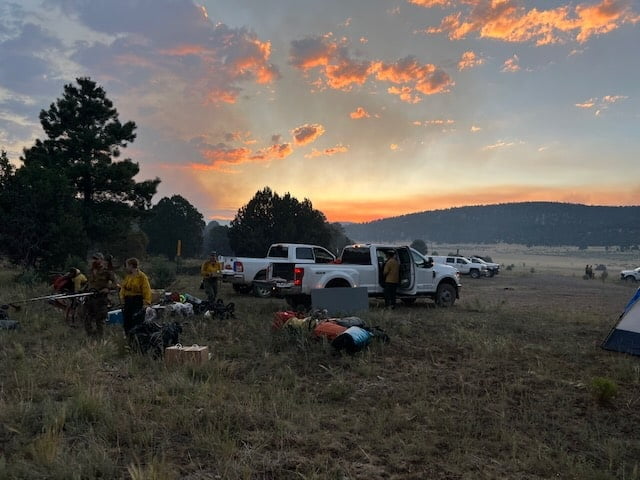 A field at sunset with people, trucks, and tents.