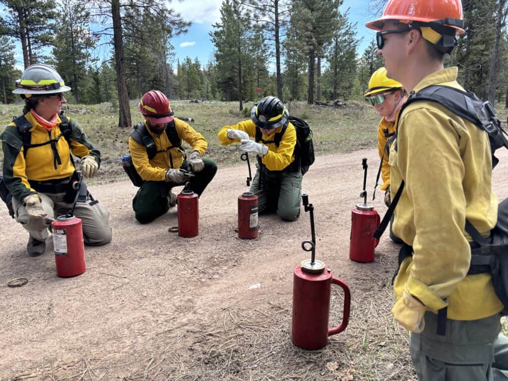 Firefighters gather in a circle to fill drip torches with fuel.